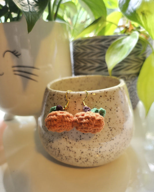 Crocheted carrot decoration on a ceramic cup with a cat design, surrounded by green plants.