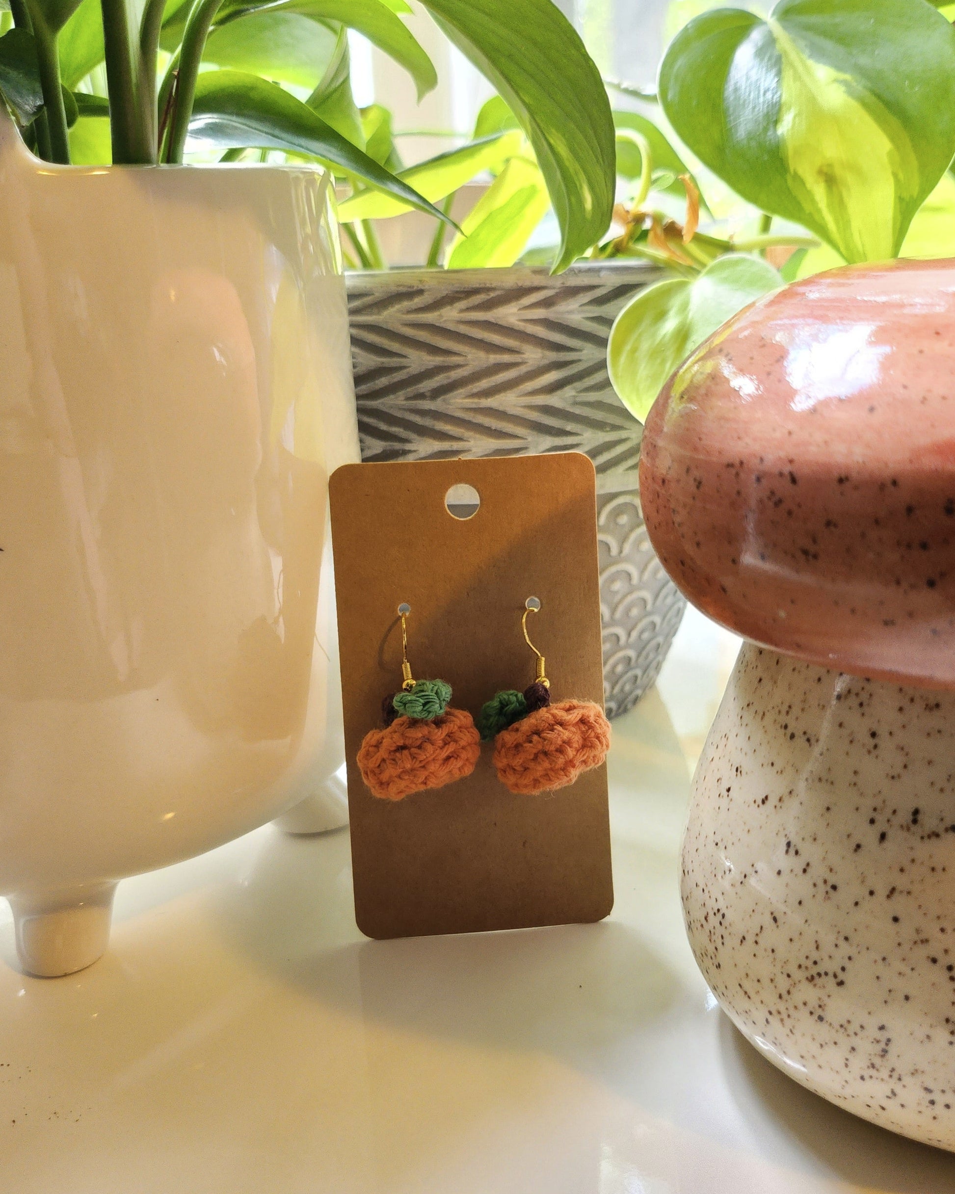 Crochet earrings on a card with potted plants in the background