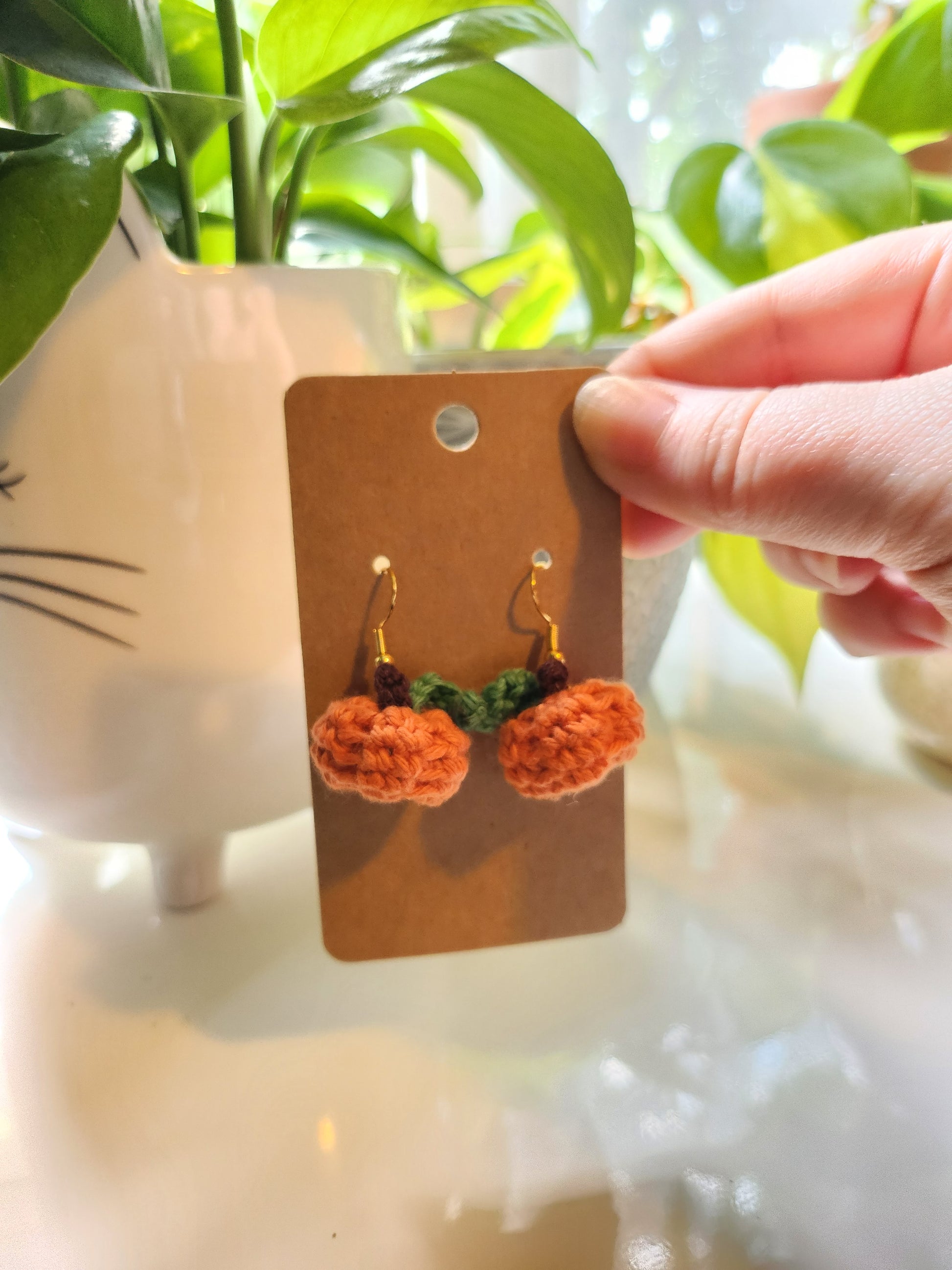 Hand holding a card with pumpkin earrings on a blurred background