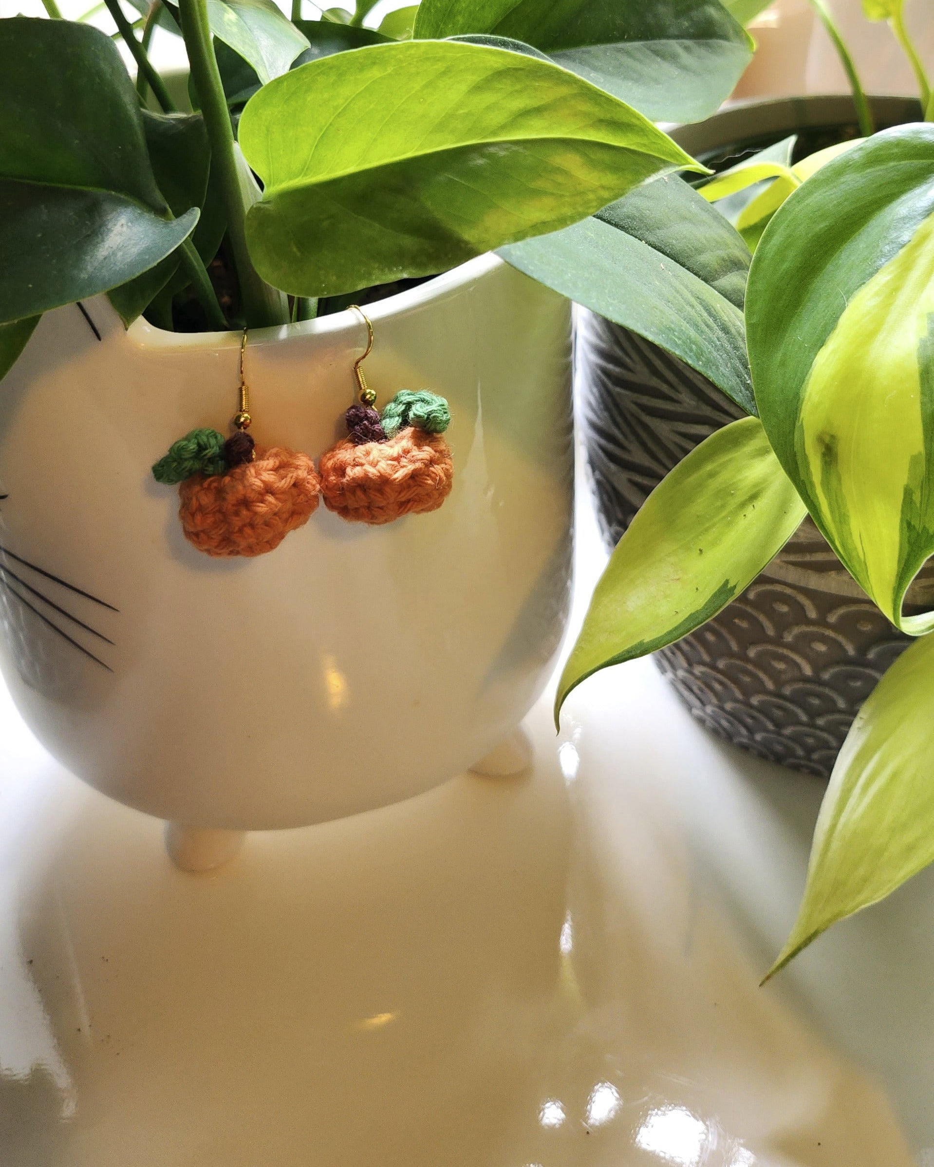 Pair of pumpkin earrings with green leaves displayed in a white.