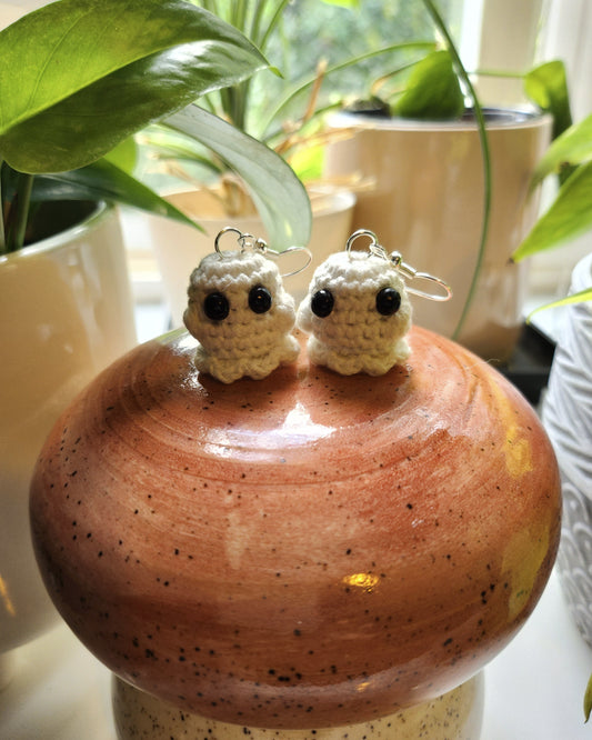 Ghost earrings sitting on a mushroom ceramic surrounded by plants.