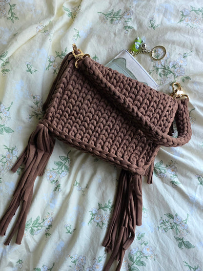 Brown crocheted bag with tassels on a floral fabric background