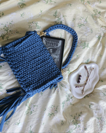 Blue crocheted bag with tassels on a floral bedspread