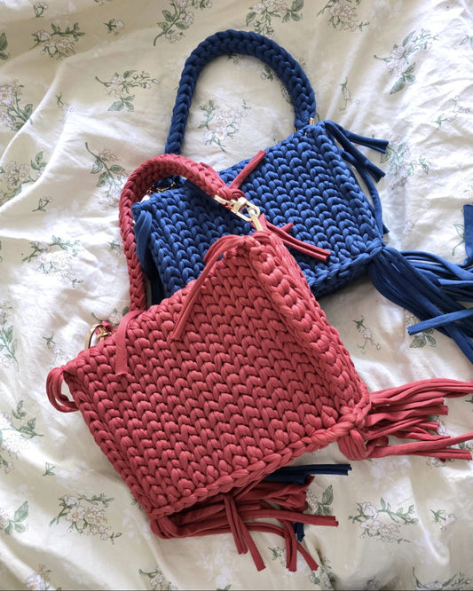 Two crochet bags, one blue and one red, on a floral fabric background.