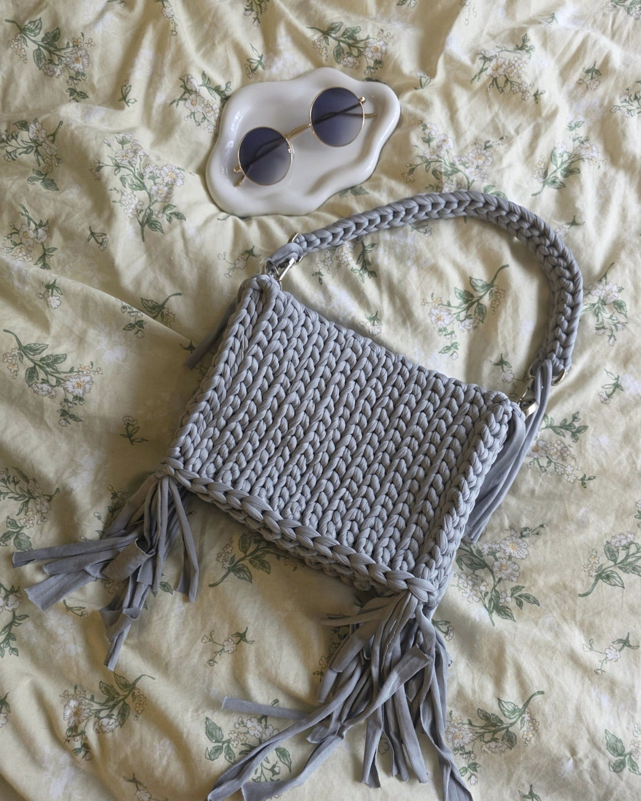 Gray crocheted bag with tassels on a floral bedspread