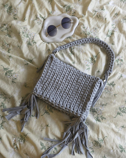 Gray crocheted bag with tassels on a floral bedspread