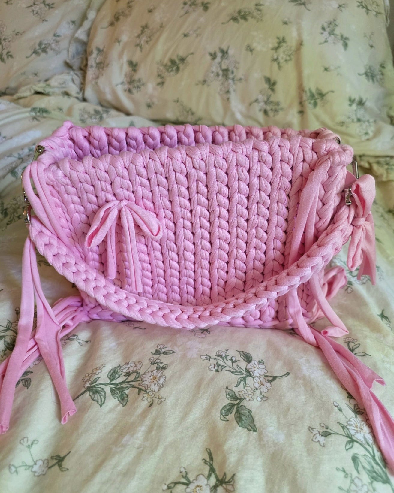 Pink crocheted bag with tassels on a floral-patterned fabric background