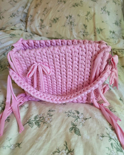 Pink crocheted bag with tassels on a floral-patterned fabric background