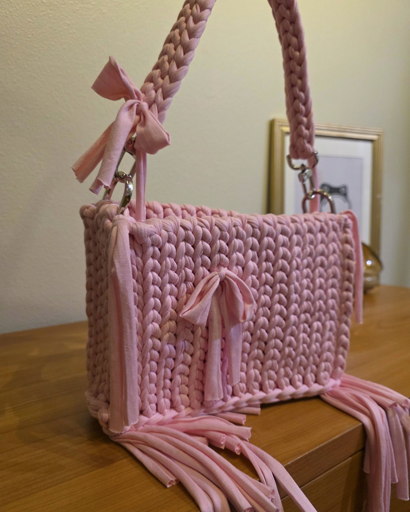 Pink crocheted bag with tassels on a wooden surface