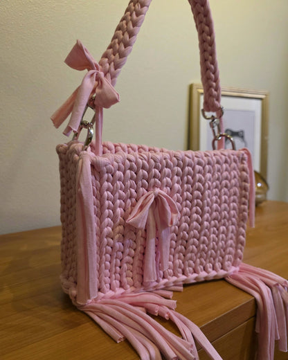 Pink crocheted bag with tassels on a wooden surface