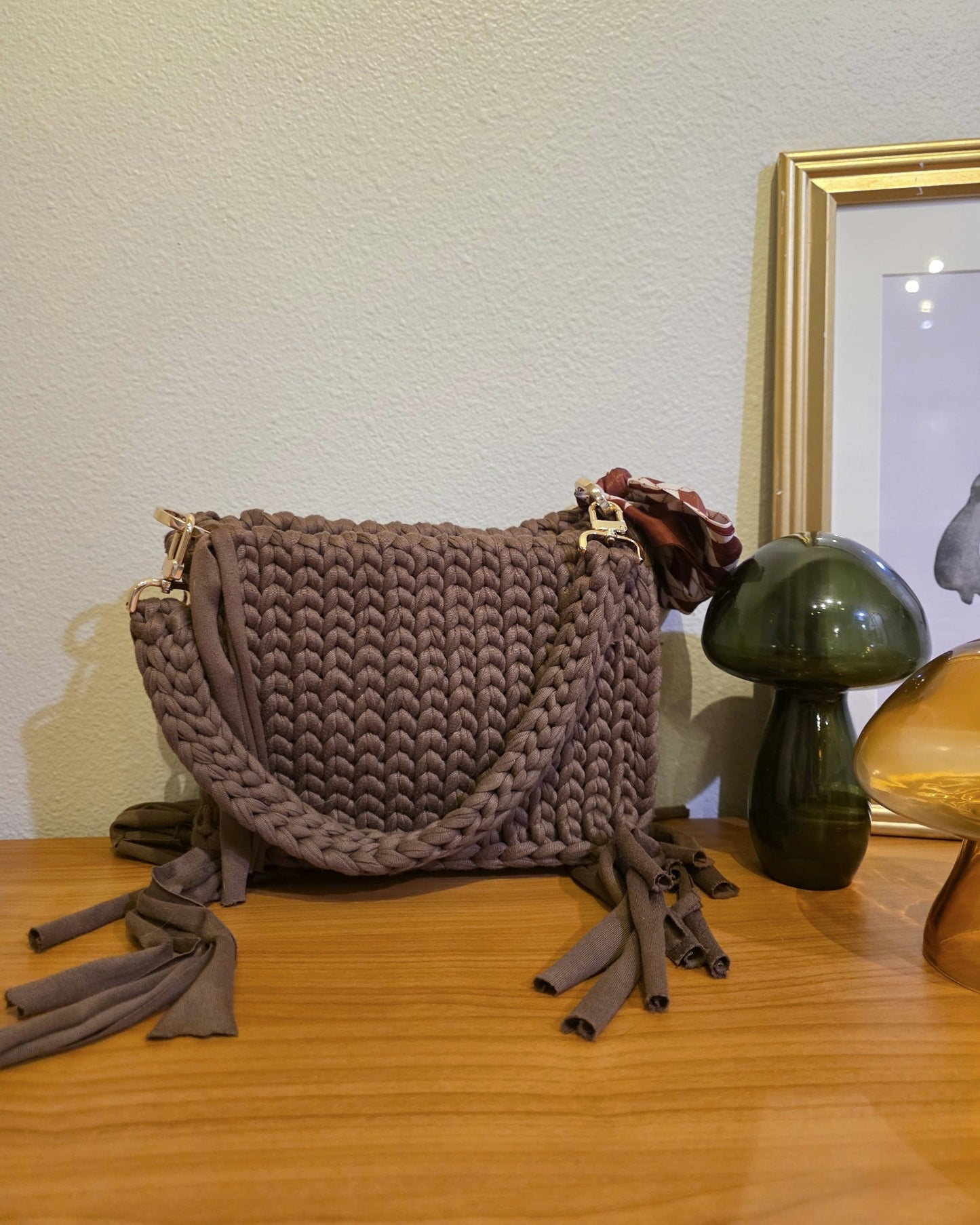 Brown crocheted bag hanging on a wooden surface.