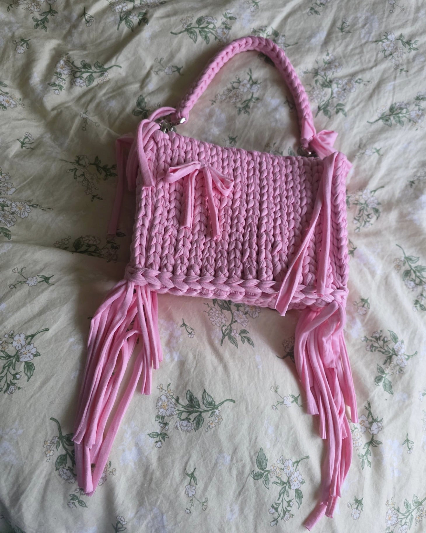 Pink crocheted bag with tassels on a floral bedspread